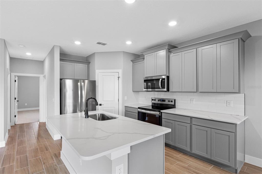A modern kitchen features gray cabinets, white quartz countertops, stainless steel appliances, and wood-look flooring — 13521 WALDEN SHEFFIELD ROAD, DOVER, FL