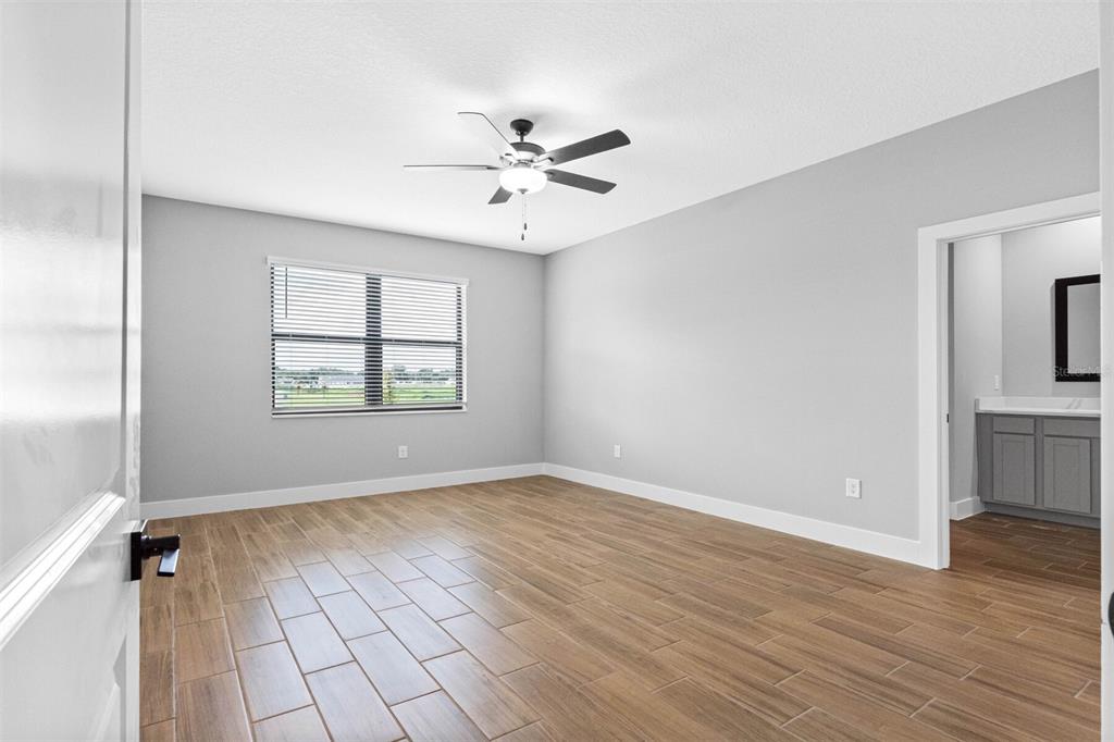 A bedroom with light gray walls, wood-look tile flooring, a ceiling fan, and an attached bathroom — 13521 WALDEN SHEFFIELD ROAD, DOVER, FL