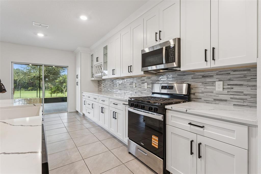 A modern kitchen features white cabinets, stainless steel appliances, quartz countertops, and a tiled backsplash — 29505 CASPIAN STREET, LEESBURG, FL