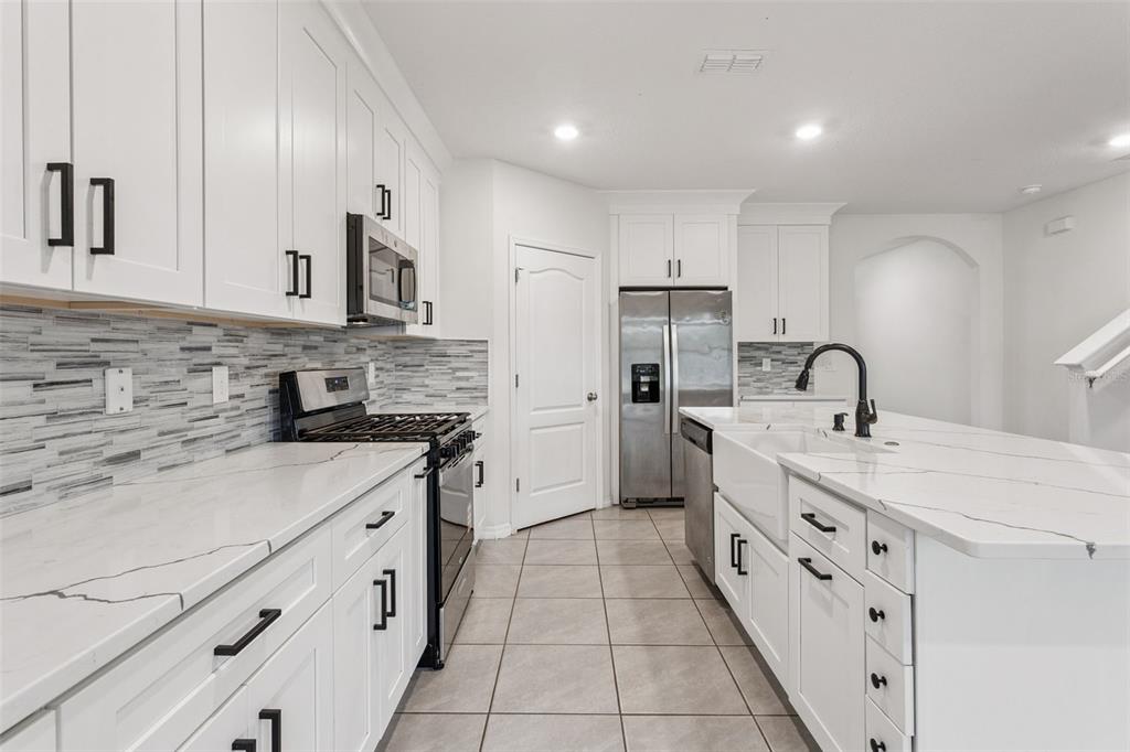 A modern kitchen features white cabinets, marble-look countertops, stainless steel appliances, and a farmhouse sink — 29505 CASPIAN STREET, LEESBURG, FL