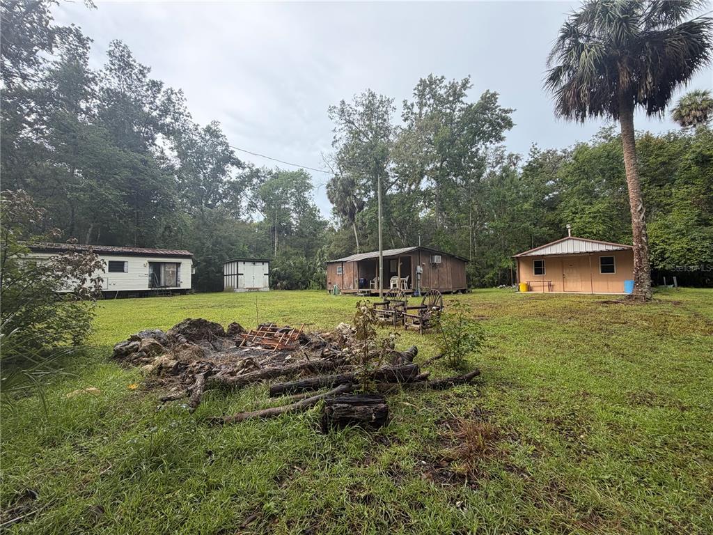 A grassy yard features a mobile home, two small wooden structures, and a fire pit — 17850 SE 32ND TERRACE, INGLIS, FL