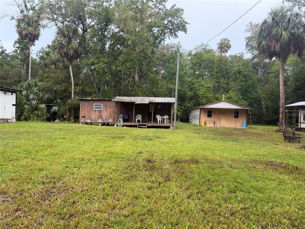 A grassy yard features a weathered wooden cabin with a porch beside a tan shed — 17850 SE 32ND TERRACE, INGLIS, FL