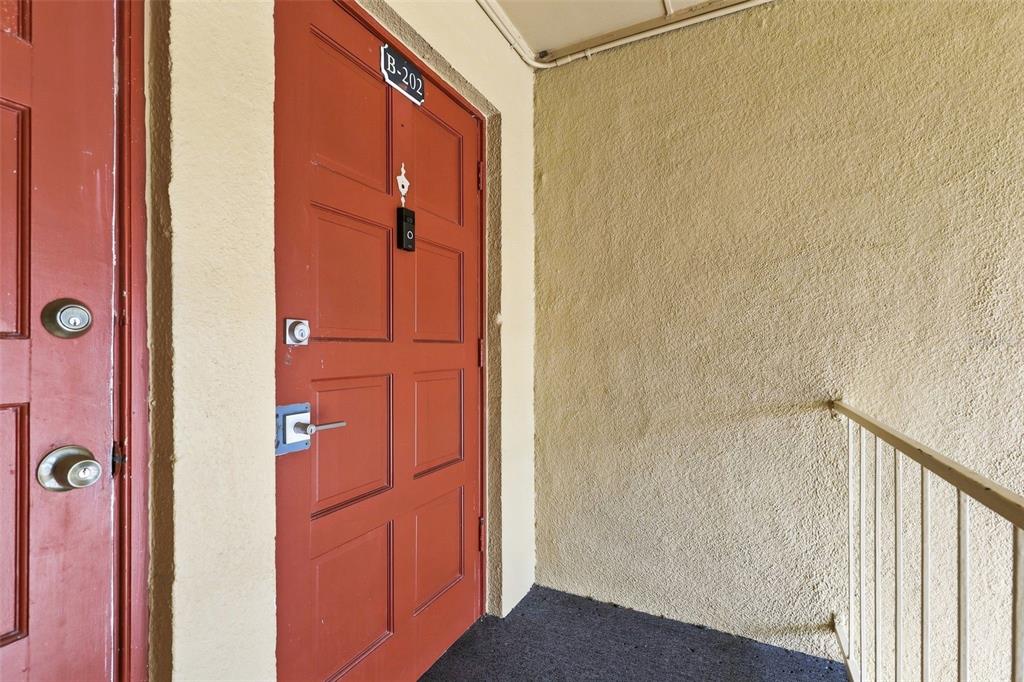 A red apartment door labeled B-202 sits next to a textured wall and metal railing — 1000 LAKE OF THE WOODS BOULEVARD UNIT B202, FERN PARK, FL