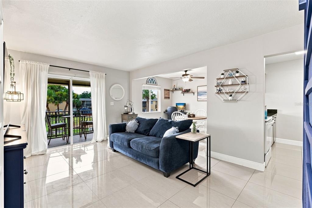 A living room features a blue sofa, tile flooring, and a sliding glass door to a balcony — 1000 LAKE OF THE WOODS BOULEVARD UNIT B202, FERN PARK, FL