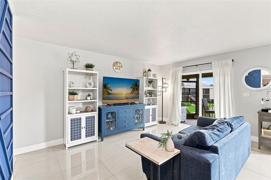 A living room features a blue sofa, a television on a blue console, and white shelving — 1000 LAKE OF THE WOODS BOULEVARD UNIT B202, FERN PARK, FL