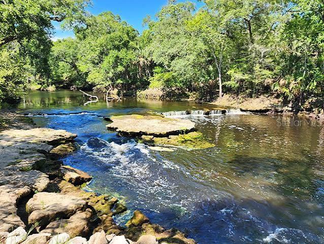 A small river flows over rocky ledges surrounded by a lush green forest — 507 4TH STREET NW, STEINHATCHEE, FL