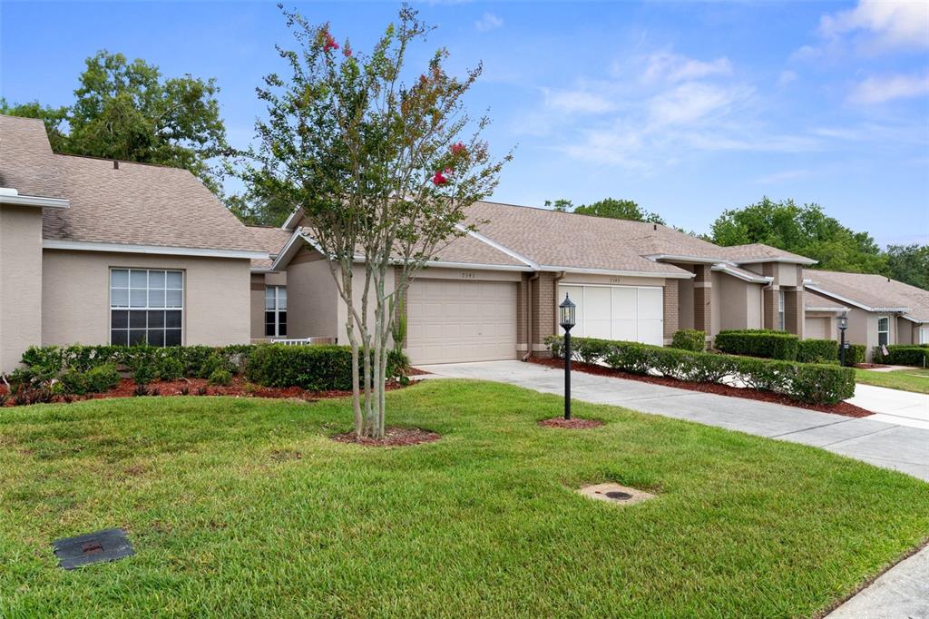 A single-story suburban house with a tan exterior, two-car garage, and a manicured front lawn — 7343 WILLOW BROOK DRIVE, SPRING HILL, FL