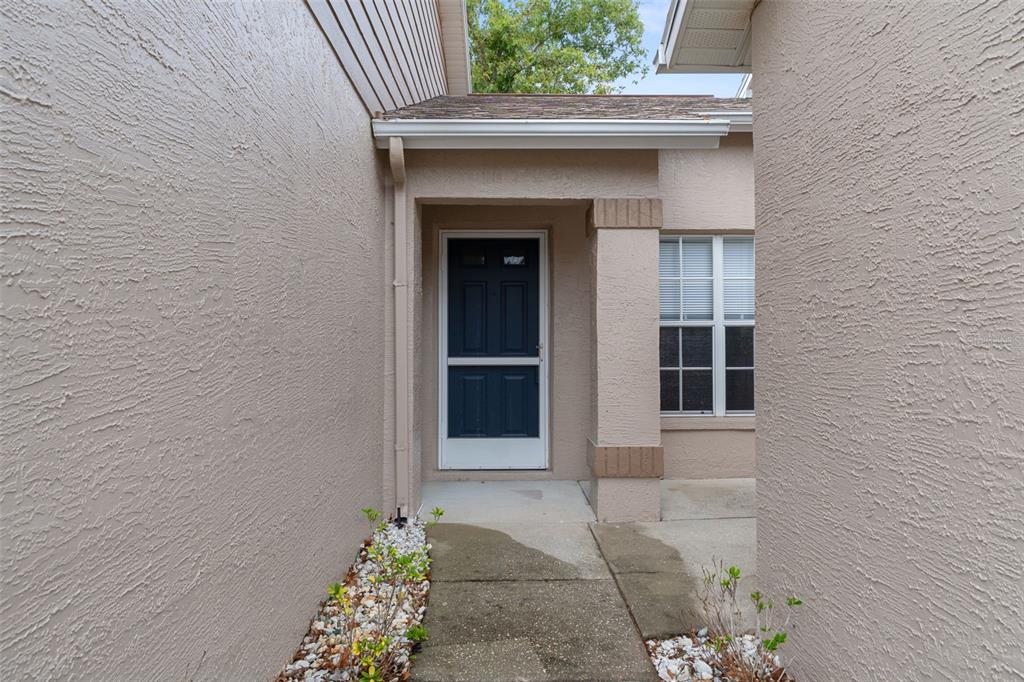 A concrete walkway leads to a dark blue front door under a covered entryway — 7343 WILLOW BROOK DRIVE, SPRING HILL, FL