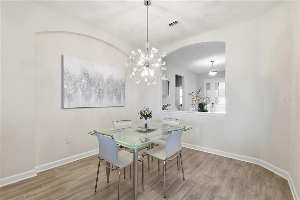 A dining room features a glass table, modern chandelier, and light wood-look tile flooring — 1077 DOWNSWING PL, DAVENPORT, FL