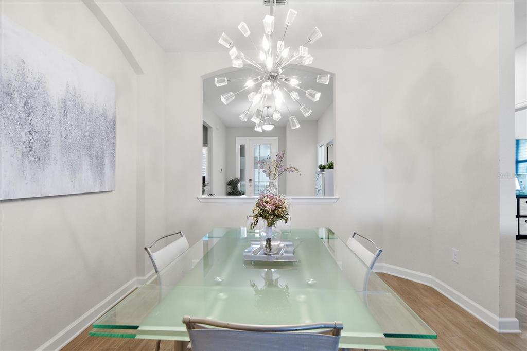 A dining room features a glass table, modern chandelier, and a large wall art piece — 1077 DOWNSWING PL, DAVENPORT, FL