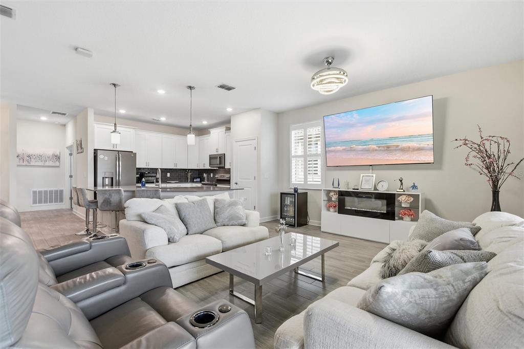 An open-concept living room and kitchen featuring white cabinetry, gray flooring, and a wall-mounted television — 1077 DOWNSWING PL, DAVENPORT, FL