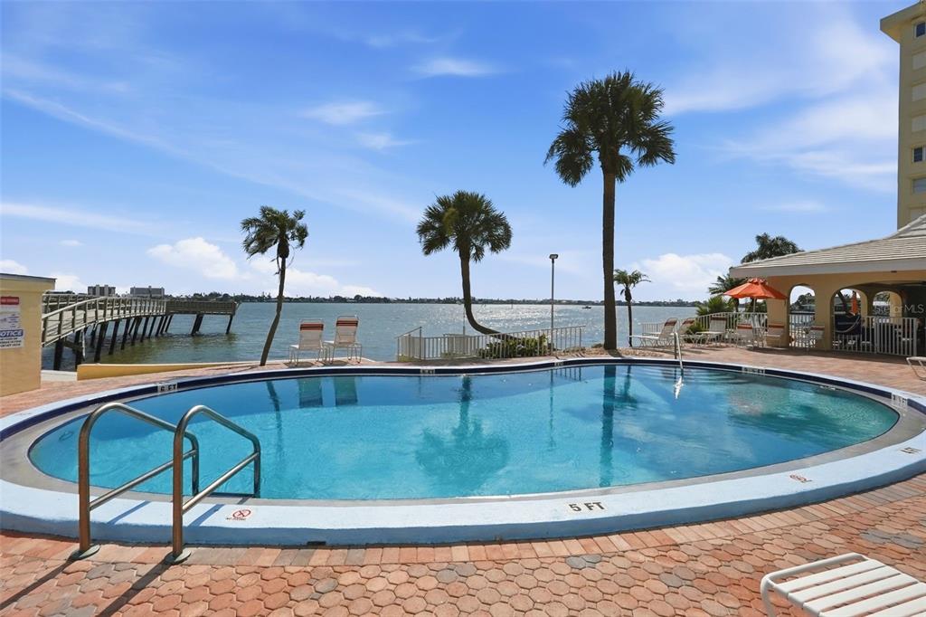 A swimming pool sits on a brick patio overlooking a pier and the ocean — 4775 COVE CIRCLE UNIT 606, ST PETERSBURG, FL