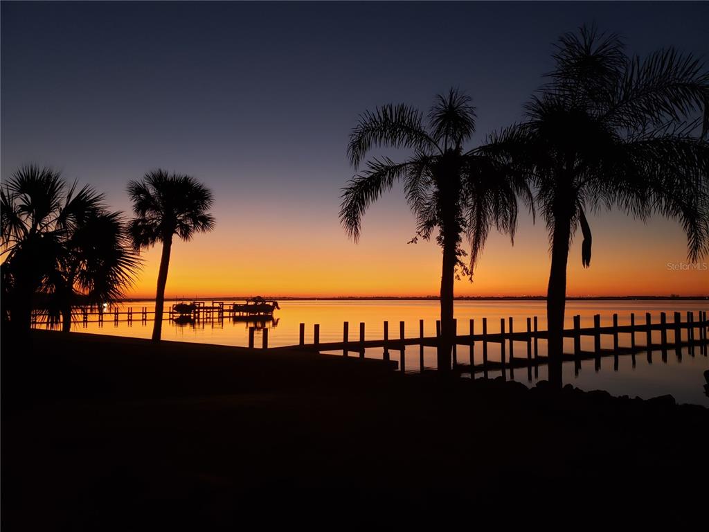 A silhouette of palm trees and a wooden dock overlooks a calm lake at sunset — 24181 HARBORVIEW ROAD, PUNTA GORDA, FL