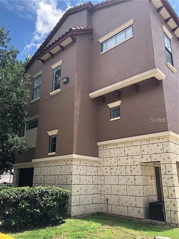 A low-angle exterior view of a multi-story brown building with stone veneer on the ground level — 6129 METROWEST BOULEVARD UNIT 101, ORLANDO, FL