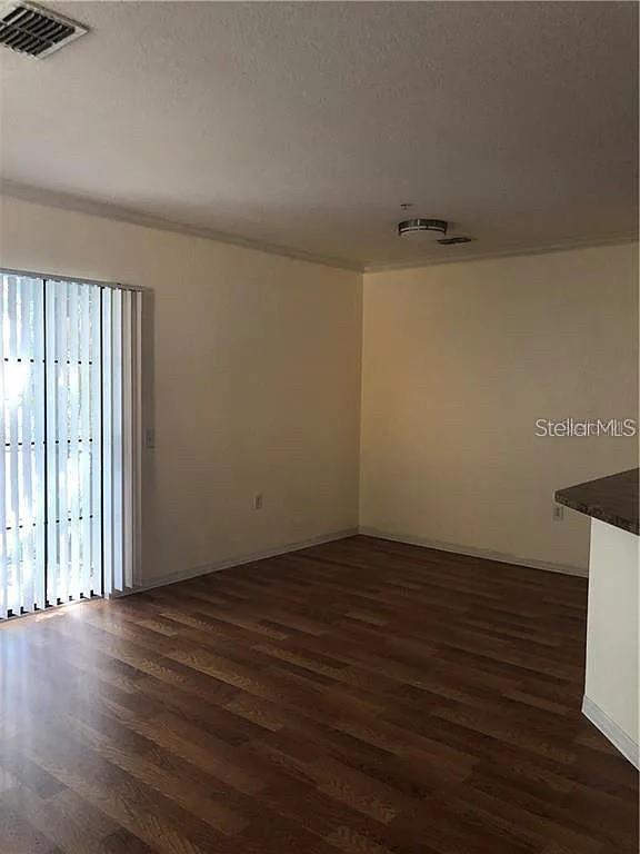 An empty room features wood-look flooring, beige walls, and a sliding glass door with blinds — 6129 METROWEST BOULEVARD UNIT 101, ORLANDO, FL
