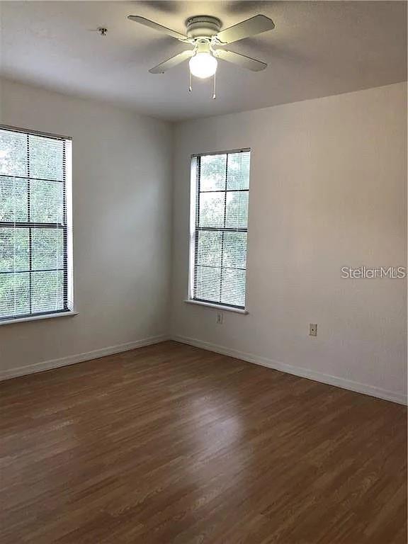 An empty room features wood-look flooring, two windows with blinds, and a ceiling fan — 6129 METROWEST BOULEVARD UNIT 101, ORLANDO, FL