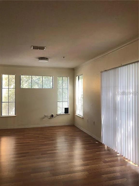 An empty living room features wood-look flooring, multiple windows with blinds, and vertical patio blinds — 6129 METROWEST BOULEVARD UNIT 101, ORLANDO, FL