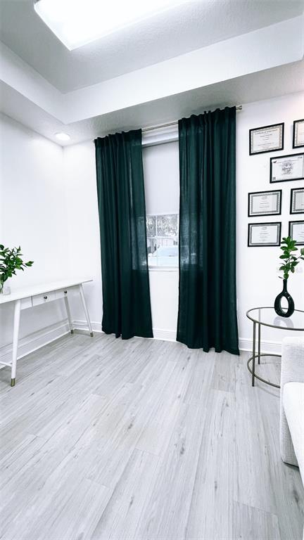 A bright office room features light wood-look flooring, dark green curtains, and a white desk — 27551 CASHFORD CIRCLE UNIT 101, WESLEY CHAPEL, FL