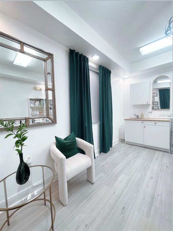 A small room features a white chair, green curtains, a mirror, and a kitchenette — 27551 CASHFORD CIRCLE UNIT 101, WESLEY CHAPEL, FL