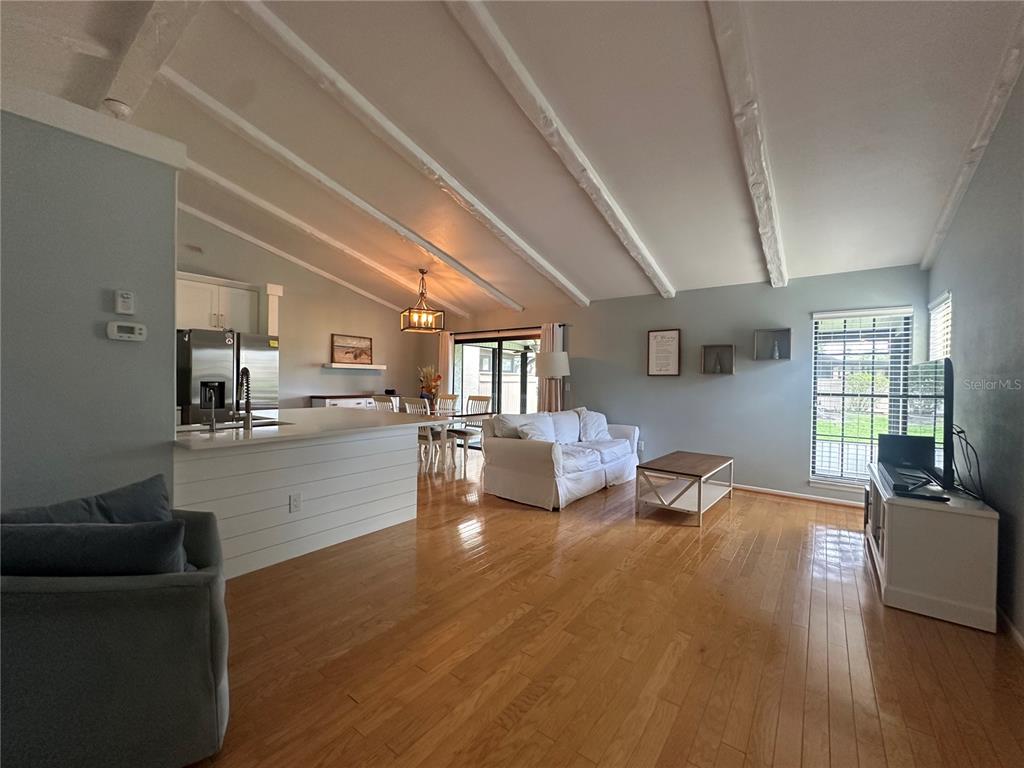 An open-concept living and dining room features vaulted ceilings with exposed beams and hardwood floors — 5736 BEAUMONT LOOP, NORTH PORT, FL