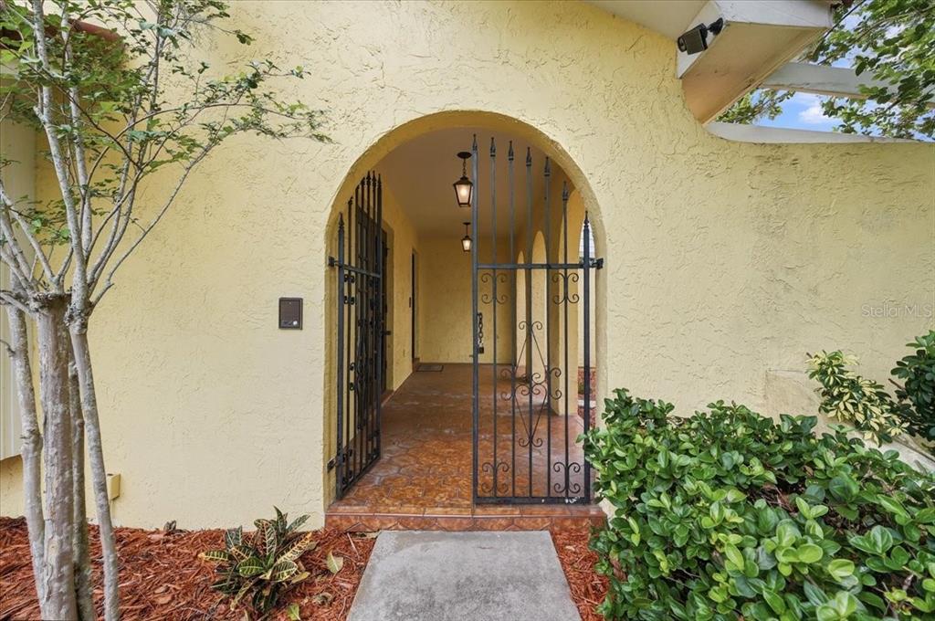 A yellow stucco house exterior features an arched entryway with a black metal gate — 7026 WILLOW RUN LOOP, LAKELAND, FL