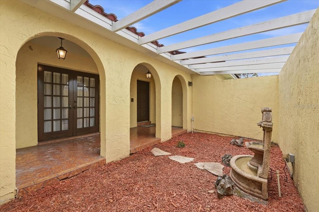 An arched entryway features a black wrought iron gate leading to a tiled porch — 7026 WILLOW RUN LOOP, LAKELAND, FL