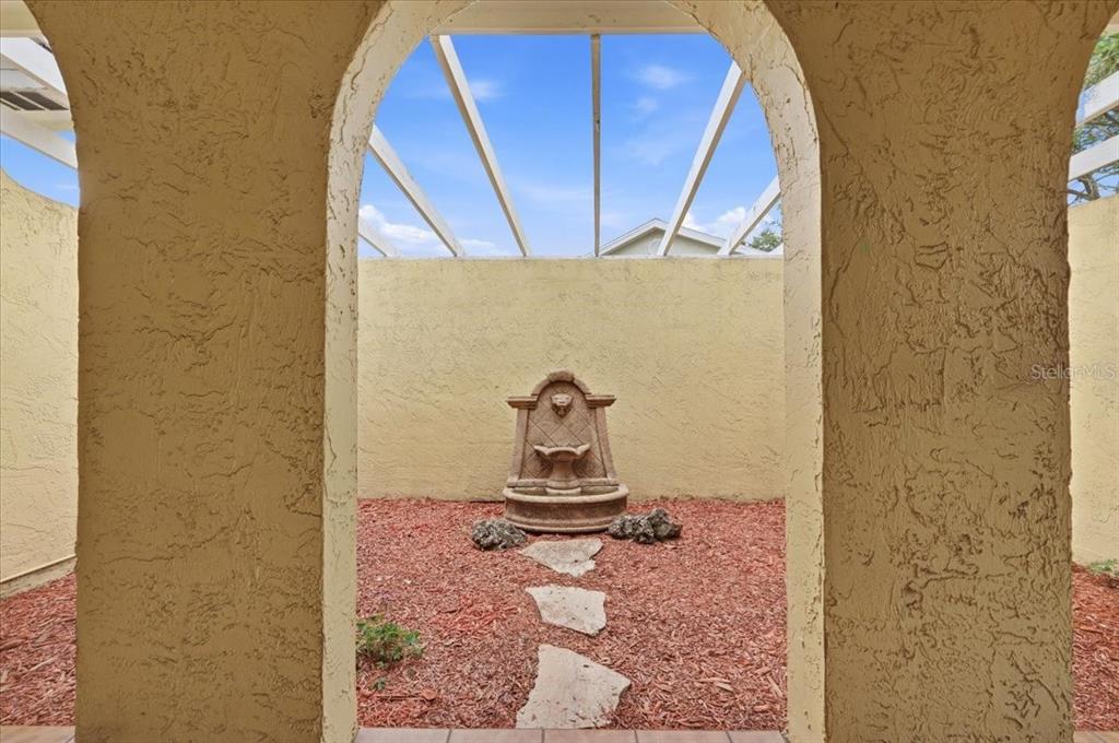 A courtyard features a stone fountain, a pergola, and arched entryways with tiled flooring — 7026 WILLOW RUN LOOP, LAKELAND, FL