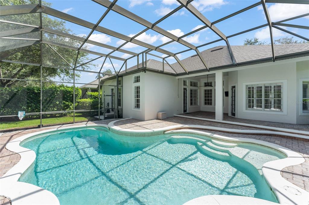A swimming pool with a sun shelf sits inside a screened-in patio behind a house — 8351 BOWDEN WAY, WINDERMERE, FL