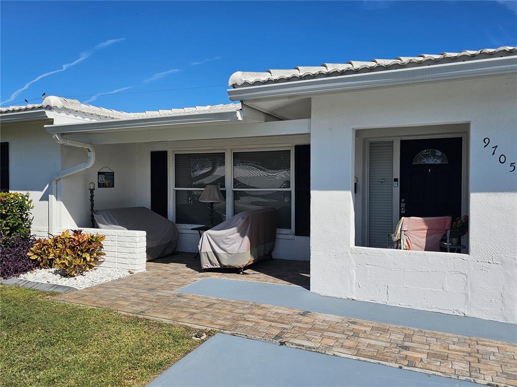 A white house exterior features a paved patio, covered furniture, and a front entryway — 9705 MAINLANDS BOULEVARD W, PINELLAS PARK, FL