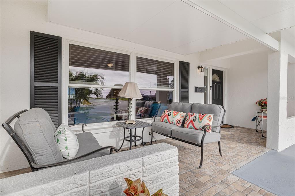 A covered patio features a brick-patterned floor, white brick wall, and outdoor seating furniture — 9705 MAINLANDS BOULEVARD W, PINELLAS PARK, FL