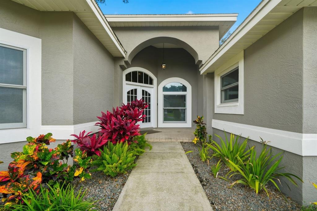 A concrete walkway leads to the arched entryway of a gray house with white trim — 700 WESTFIELD COURT, DUNEDIN, FL