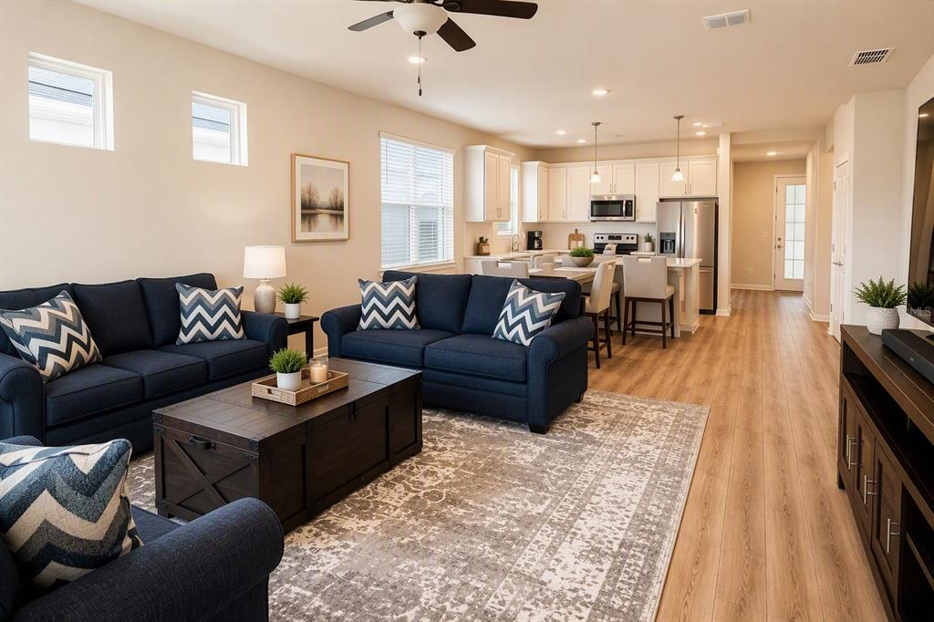 An open-concept living room and kitchen featuring dark blue sofas, wood flooring, and white cabinetry — 2756 SUMMER RETREAT LANE, KISSIMMEE, FL