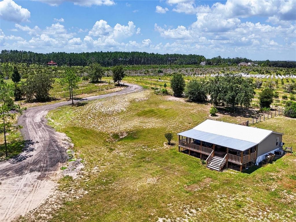 An aerial view shows a house with a metal roof and porch in a field — 37647 JENNY LANE, EUSTIS, FL