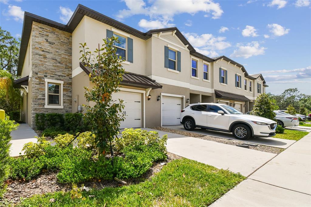 A two-story townhouse exterior with stone veneer, stucco siding, and a white SUV parked outside — 30814 VERIDIAN WAY, WESLEY CHAPEL, FL