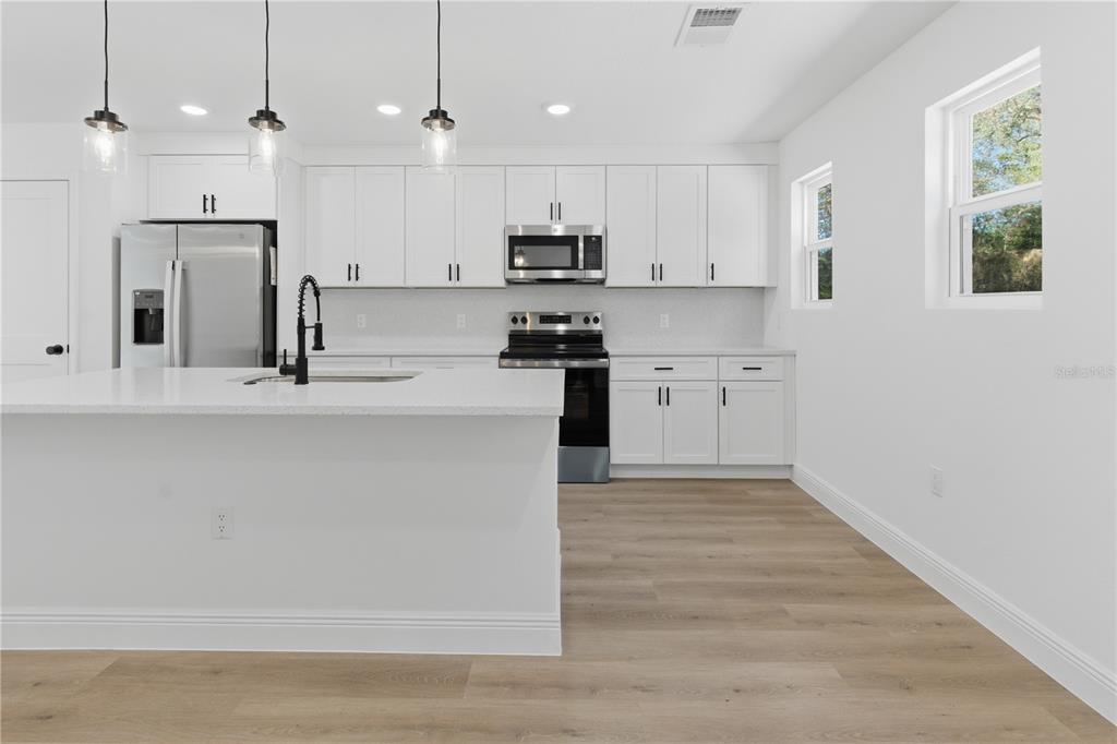 A modern kitchen features white cabinets, a central island, stainless steel appliances, and wood flooring — 727 CLEMSON DRIVE, ALTAMONTE SPRINGS, FL