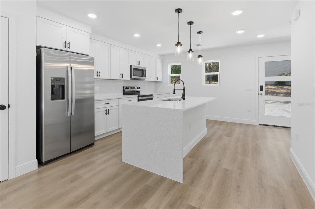 A modern kitchen features white cabinets, stainless steel appliances, a quartz island, and light flooring — 727 CLEMSON DRIVE, ALTAMONTE SPRINGS, FL