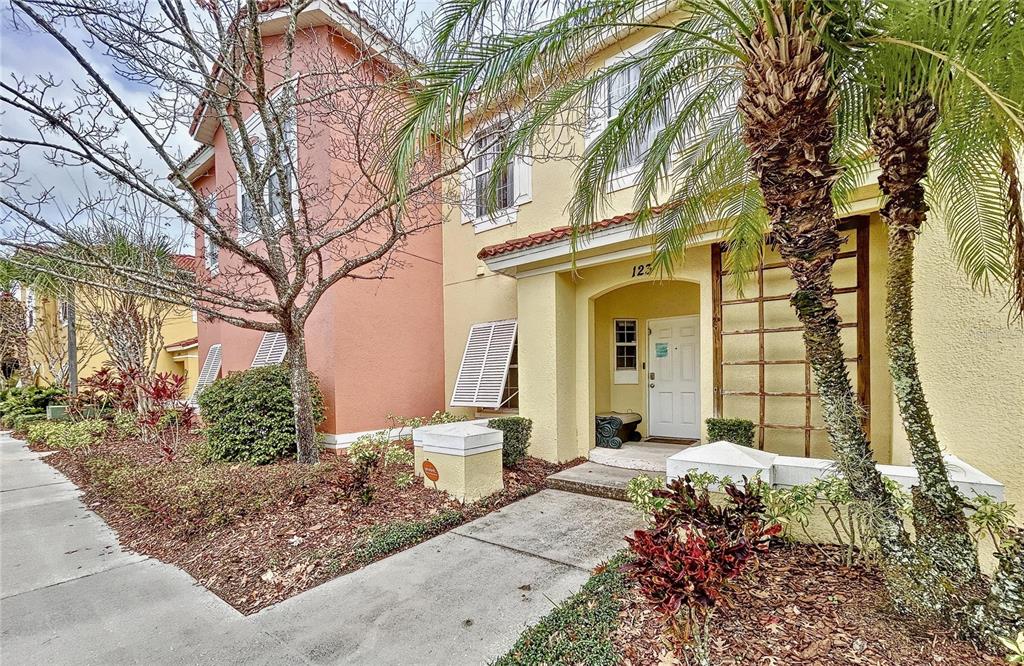 A two-story yellow and peach stucco townhouse with a palm tree and front walkway — 123 POMPANO BEACH DRIVE, KISSIMMEE, FL