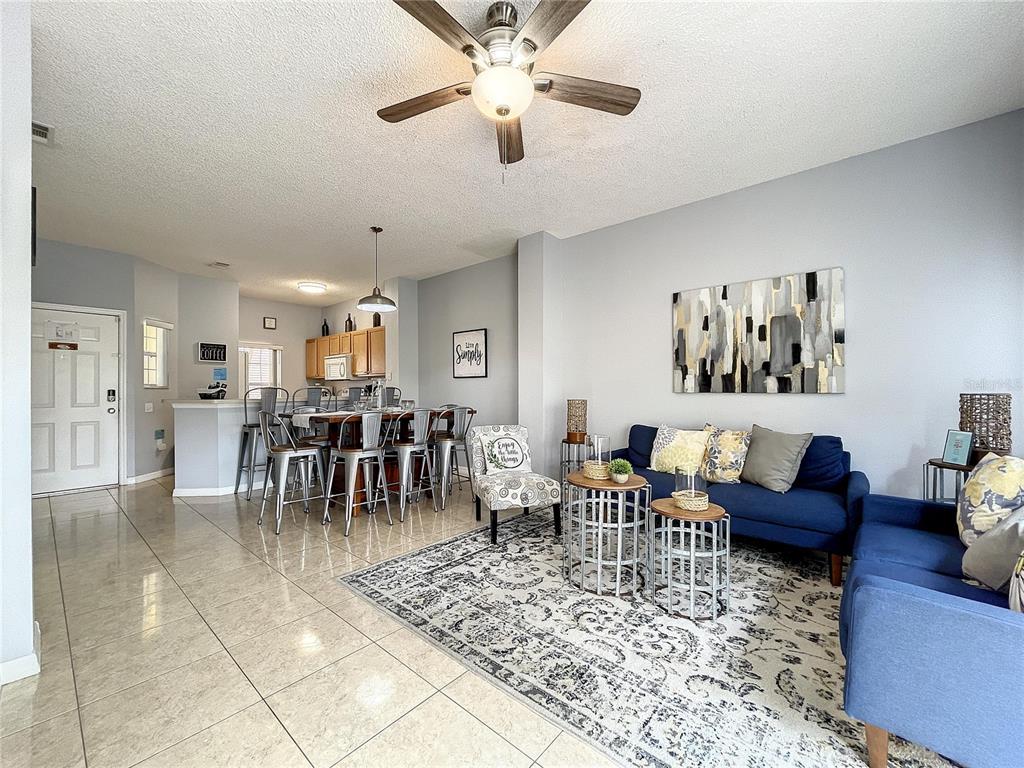 A living room with a blue sofa and dining area with metal stools on tile floors — 123 POMPANO BEACH DRIVE, KISSIMMEE, FL