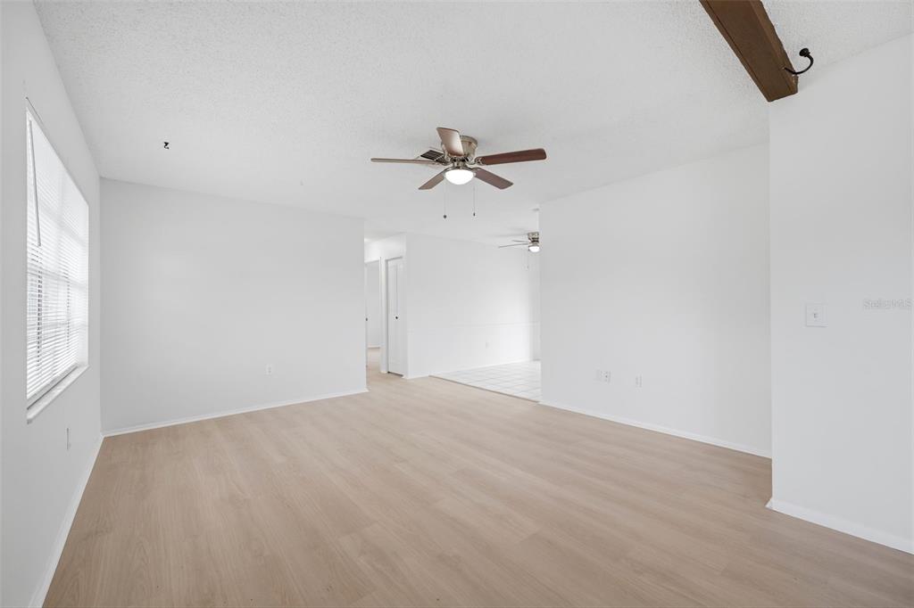 An empty living room with light wood-look flooring, white walls, and a ceiling fan — 5018 LILLILEA LANE, NEW PORT RICHEY, FL
