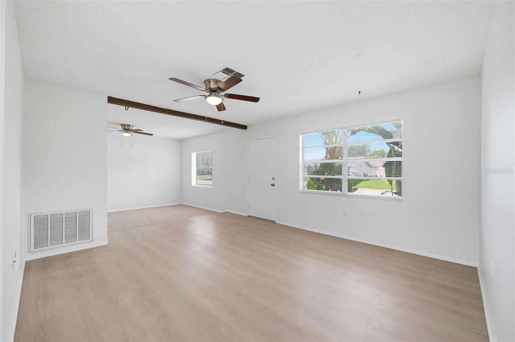 An empty living room features light wood-look flooring, white walls, and two ceiling fans — 5018 LILLILEA LANE, NEW PORT RICHEY, FL