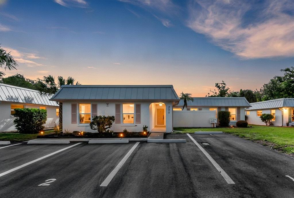 A single-story building with a metal roof and parking spaces in front at sunset — 209 BEL FOREST DRIVE UNIT 1, BELLEAIR BLUFFS, FL