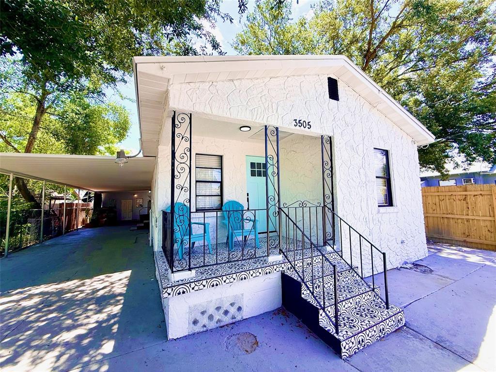 A white house with a patterned tile porch, black iron railings, and a side carport — 3505 N 16TH STREET, TAMPA, FL