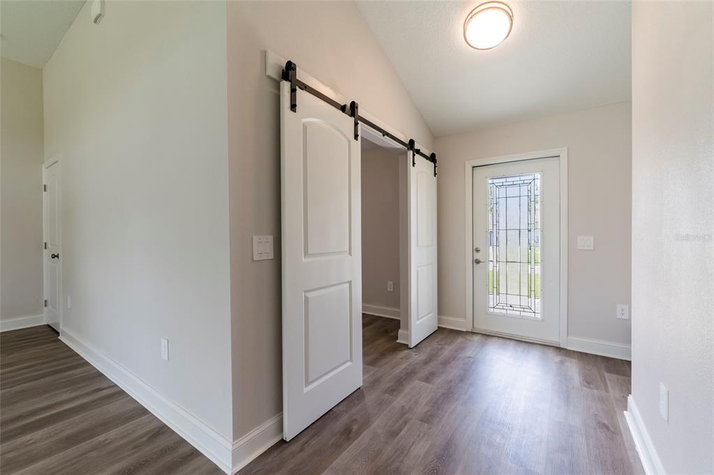 An entryway features wood-look flooring, a white front door with glass, and white sliding barn doors — 9808 SE 159TH STREET, SUMMERFIELD, FL