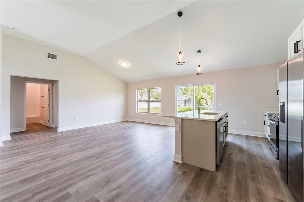 An open-concept kitchen and living area with light wood-look flooring and a kitchen island — 9808 SE 159TH STREET, SUMMERFIELD, FL