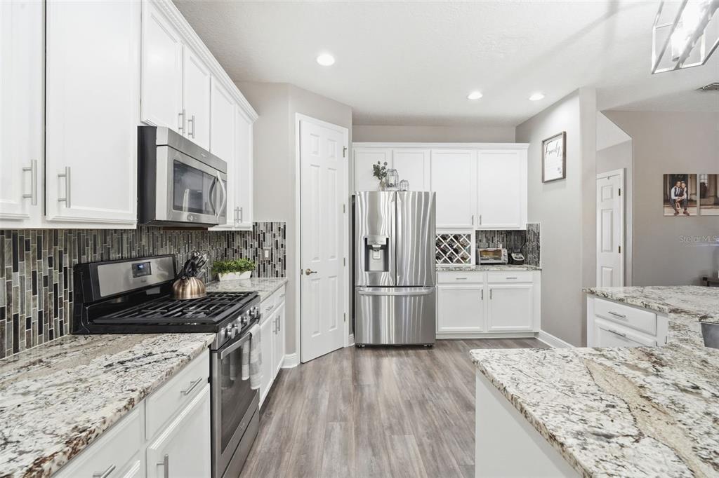 A kitchen features white cabinets, granite countertops, stainless steel appliances, and a tiled backsplash — 119 ELISSAR DRIVE, DEBARY, FL