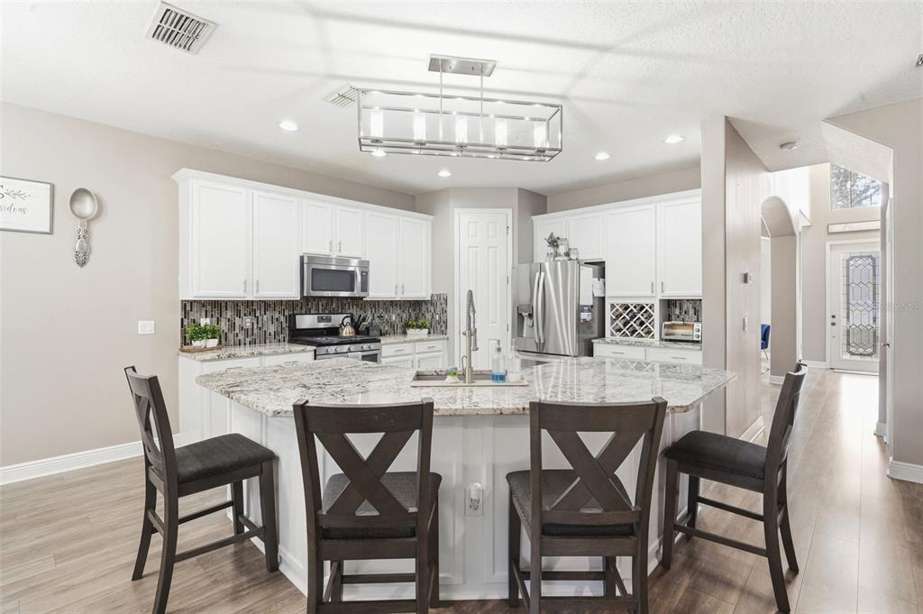 A kitchen features white cabinets, granite countertops, a large island with seating, and stainless appliances — 119 ELISSAR DRIVE, DEBARY, FL
