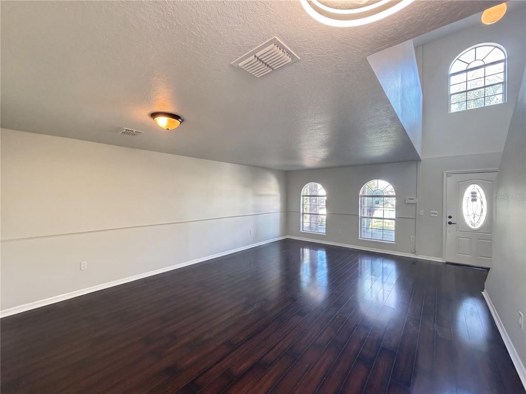 An empty living room features dark wood flooring, arched windows, and a high vaulted ceiling — 5604 ROYAL HILLS DRIVE, WINTER HAVEN, FL