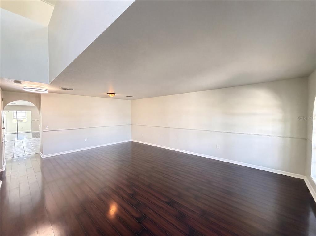 An empty room features dark wood flooring, light-colored walls with chair rail molding, and high ceilings — 5604 ROYAL HILLS DRIVE, WINTER HAVEN, FL