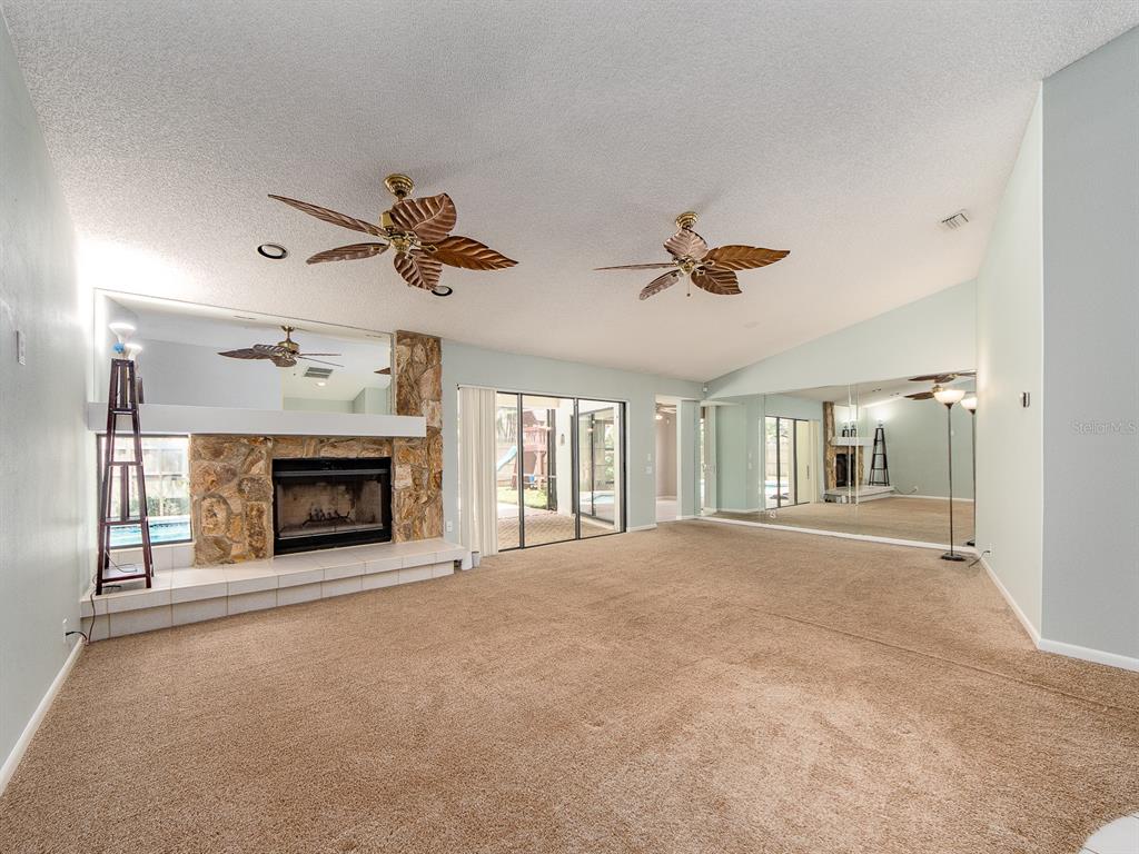 A living room features a stone fireplace, two ceiling fans, and large mirrored walls — 1612 MIDNIGHT PASS WAY, CLEARWATER, FL