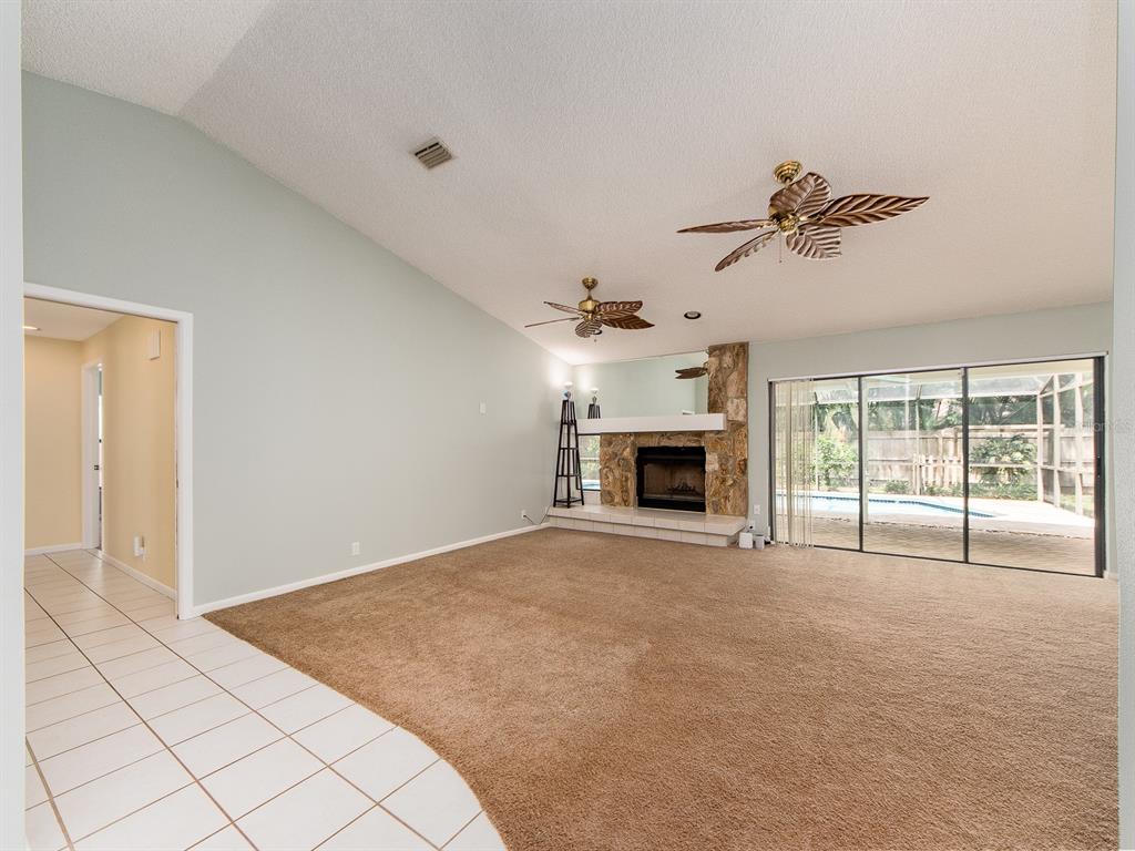A living room with carpet, a stone fireplace, ceiling fans, and sliding glass patio doors — 1612 MIDNIGHT PASS WAY, CLEARWATER, FL